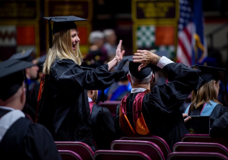 Female graduate student high-fiving a fellow graduate at commencement