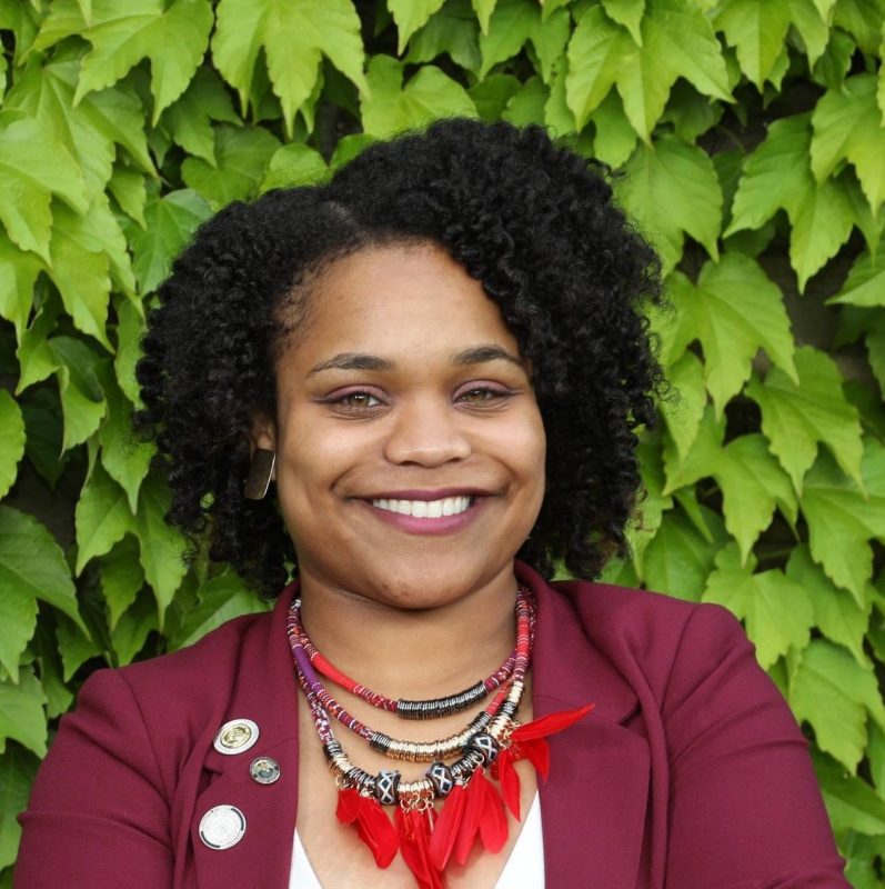 Assistant Professor Monet Roberts Monet Roberts smiles against a backdrop of Virginia creeper vine